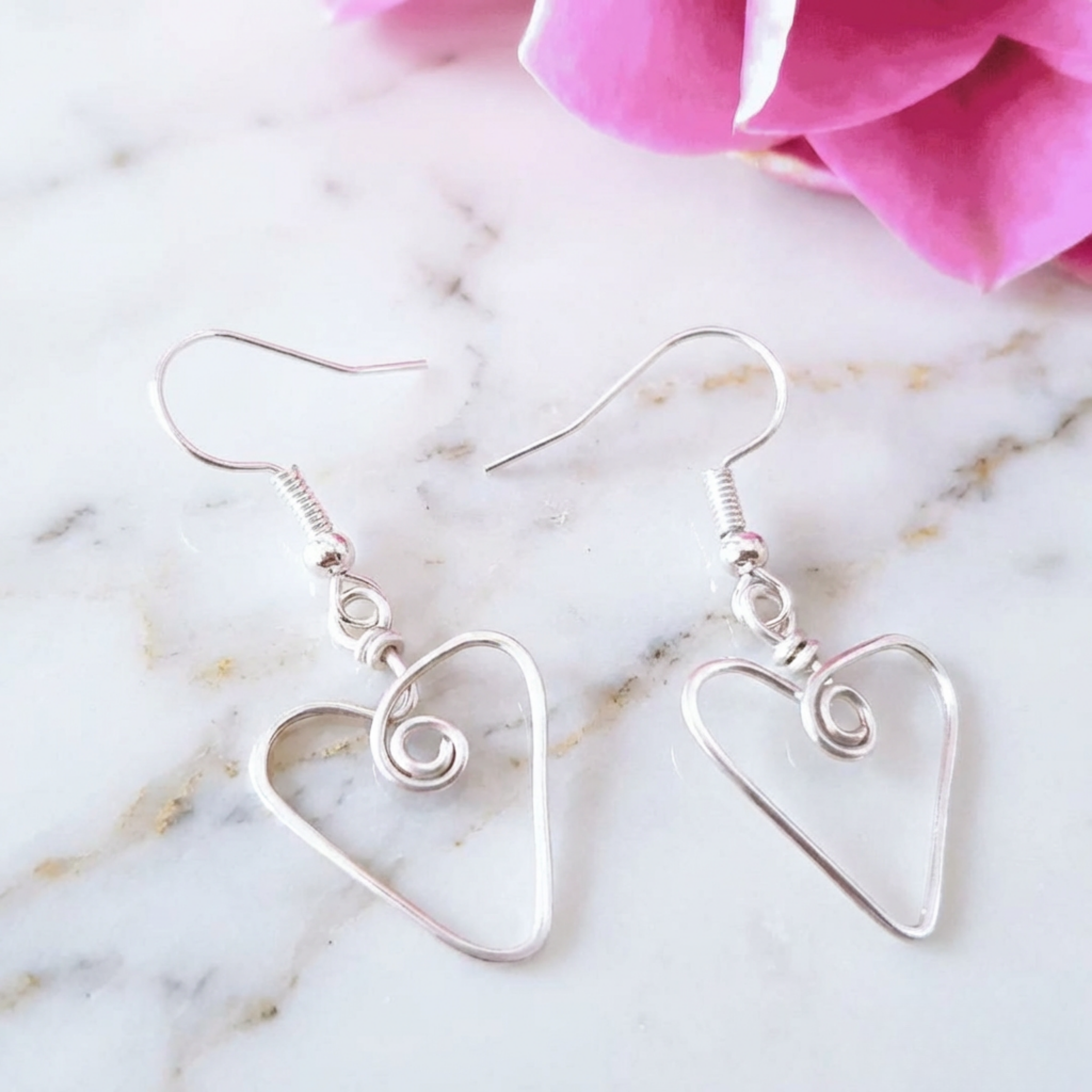 Silver heart-shaped earrings on a marble surface with pink flowers.