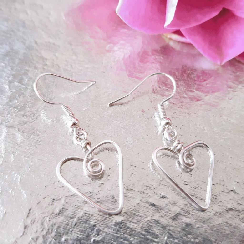 Silver heart-shaped earrings on a textured surface with a pink flower in the background