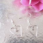 Silver heart-shaped earrings on a textured surface with a pink flower in the background