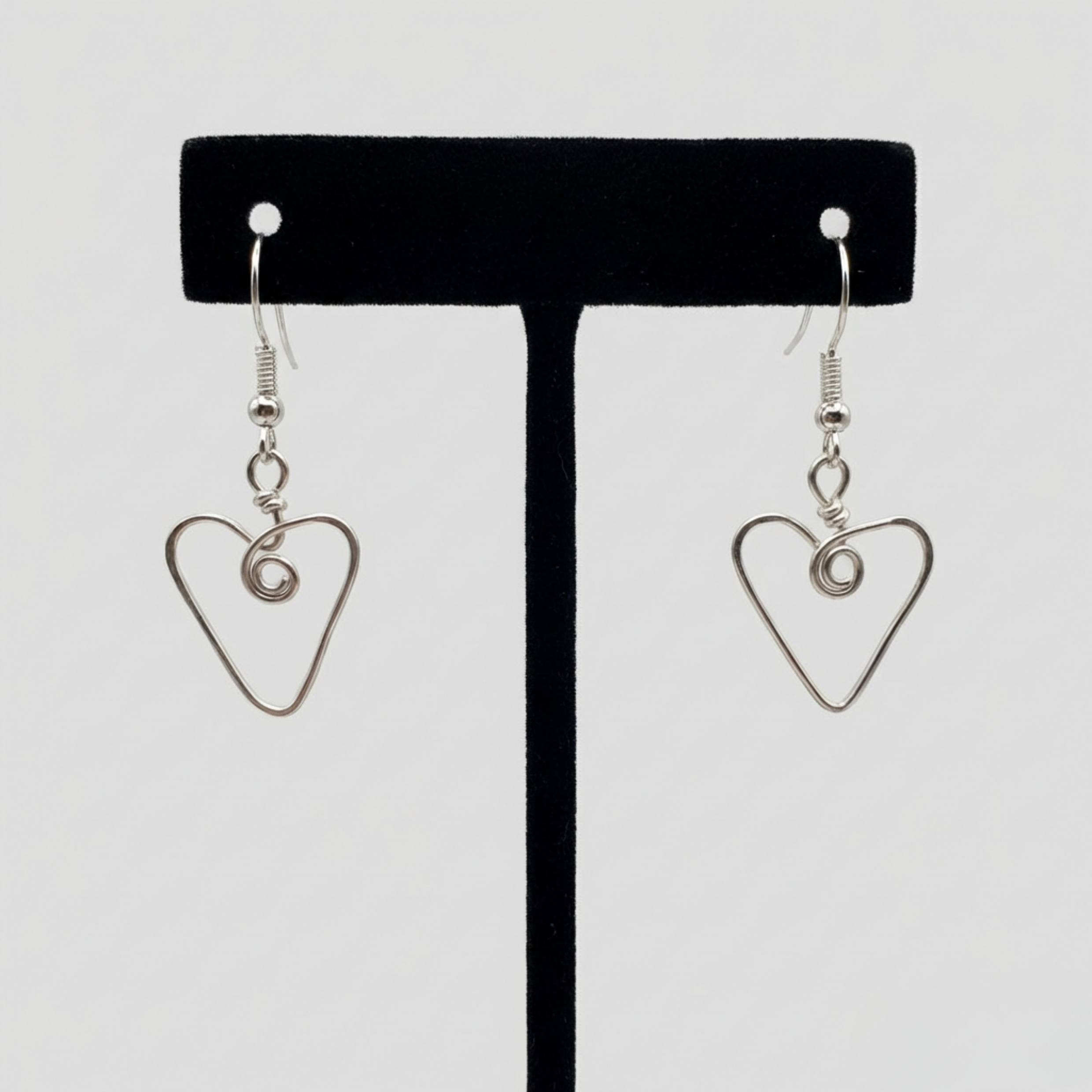 Heart-shaped earrings on a black earring stand against a white background