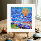 Colourful abstract artwork on a wooden easel with decorative stones on a wooden surface.