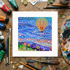 Colourful artwork of a hot air balloon in a stylized landscape on a wooden surface with art supplies.
