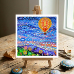 Colourful abstract artwork of a hot air balloon on a wooden easel with decorative stones and branches.