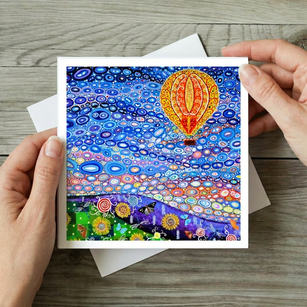 Colourful artwork of a hot air balloon and abstract patterns held by hands on a wooden surface