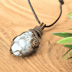 Necklace with a pendant featuring a white stone and bronze wire wrapping on a wooden surface.