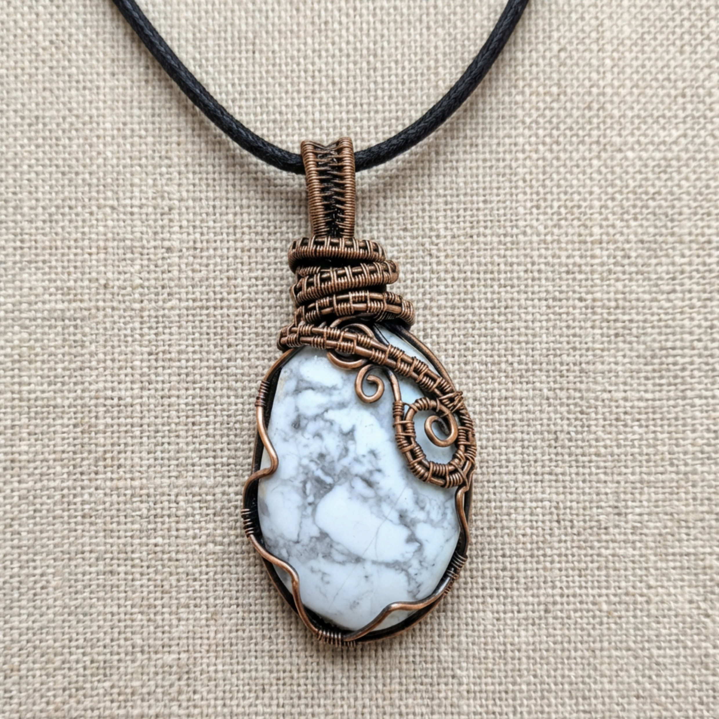 Necklace with a pendant featuring a white stone and copper wire wrapping on a beige fabric background