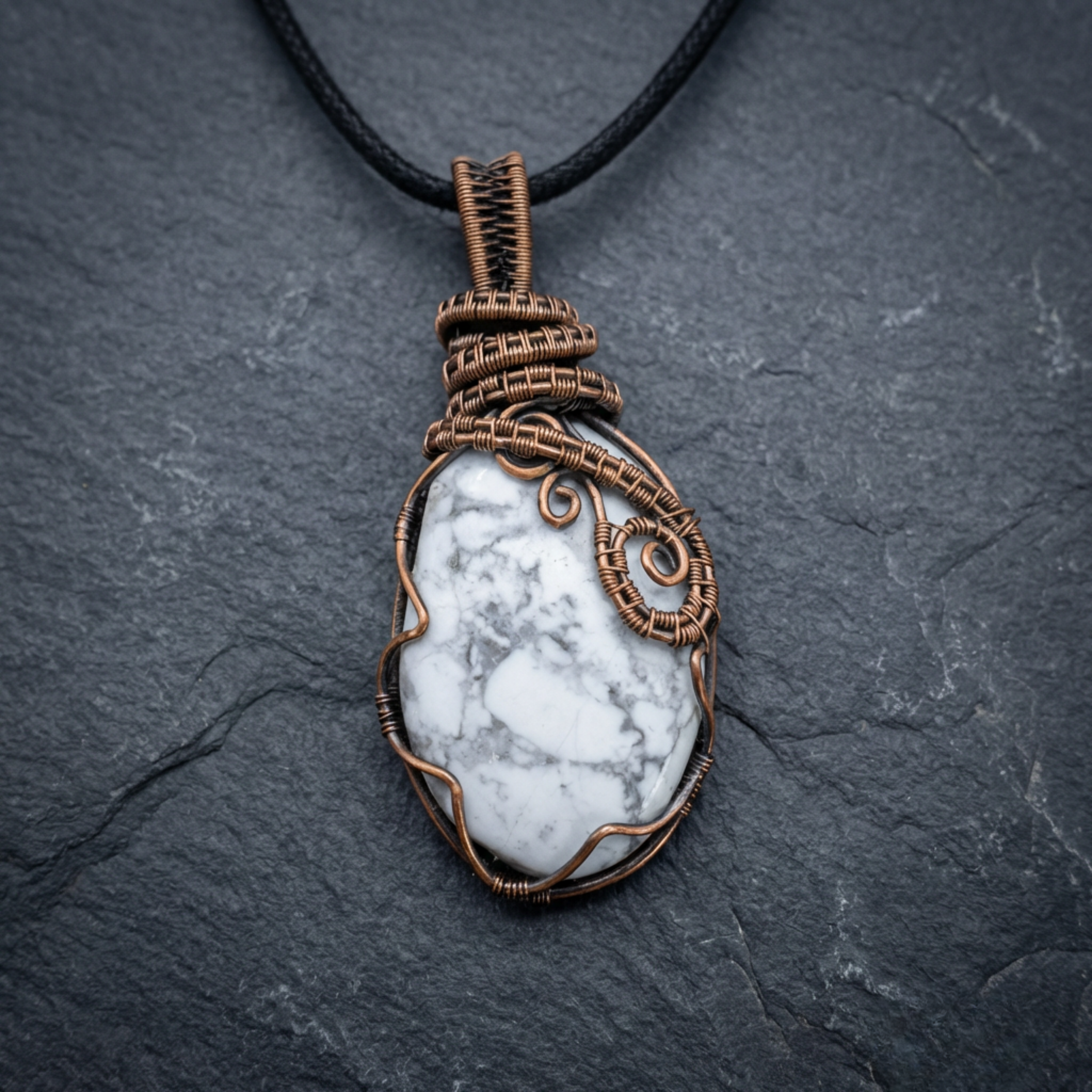 Howlite gemstone wrapped in copper wire pendant on a slate surface