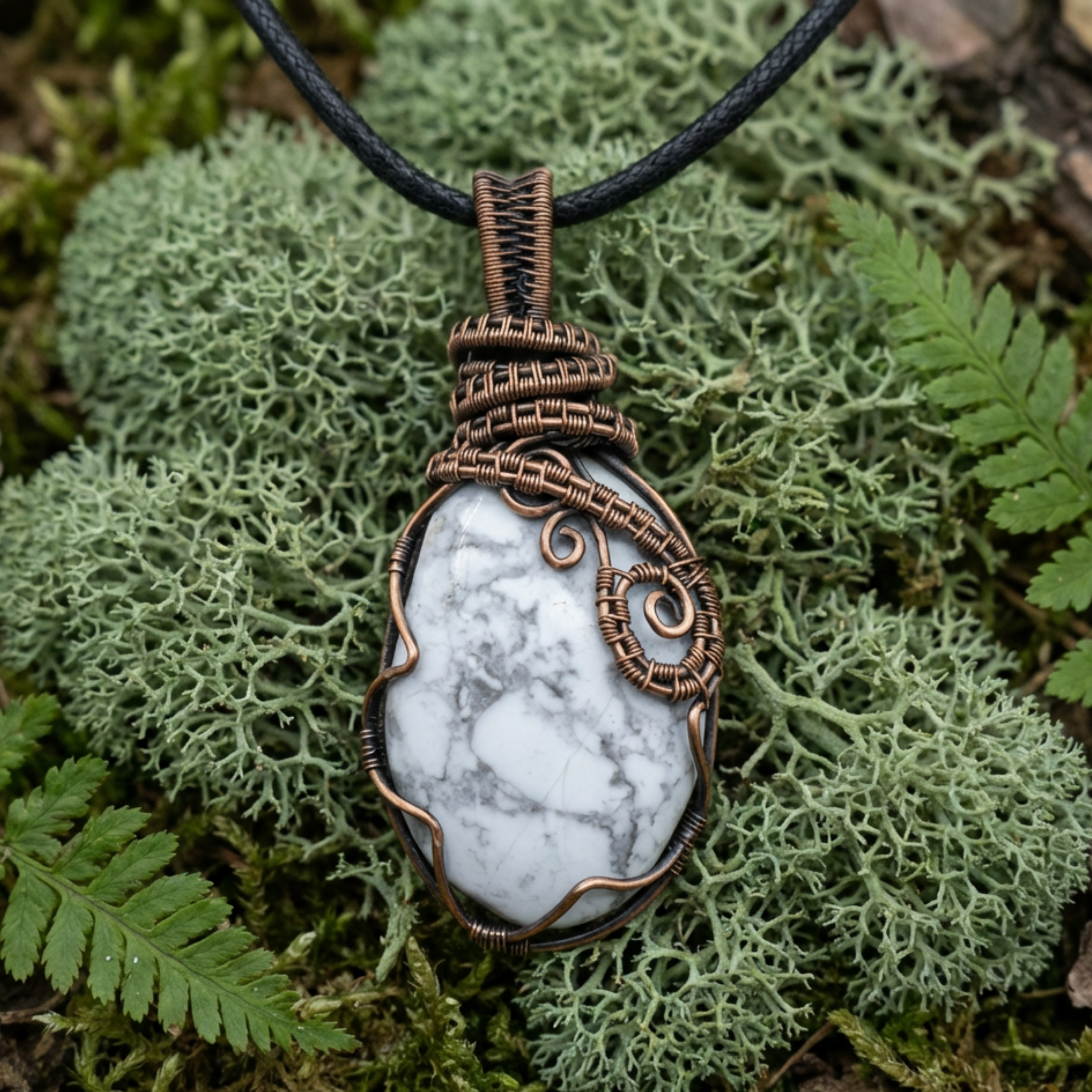 Pendant necklace with a white howlite gemstone and copper wire wrapping on a green leaf background