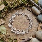 Open Silver spiral bracelet on a wooden surface with moss