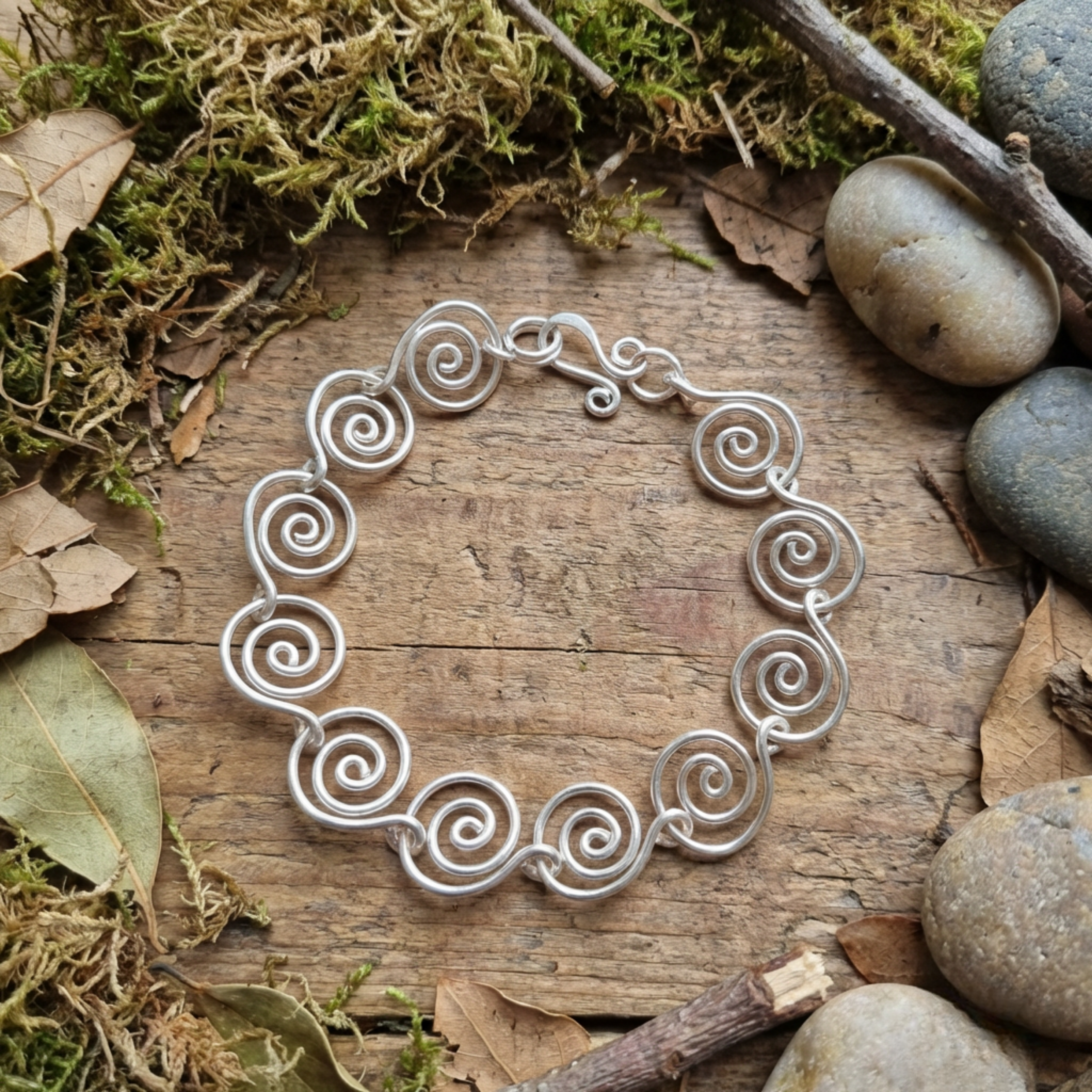 Open Silver spiral bracelet on a wooden surface with moss