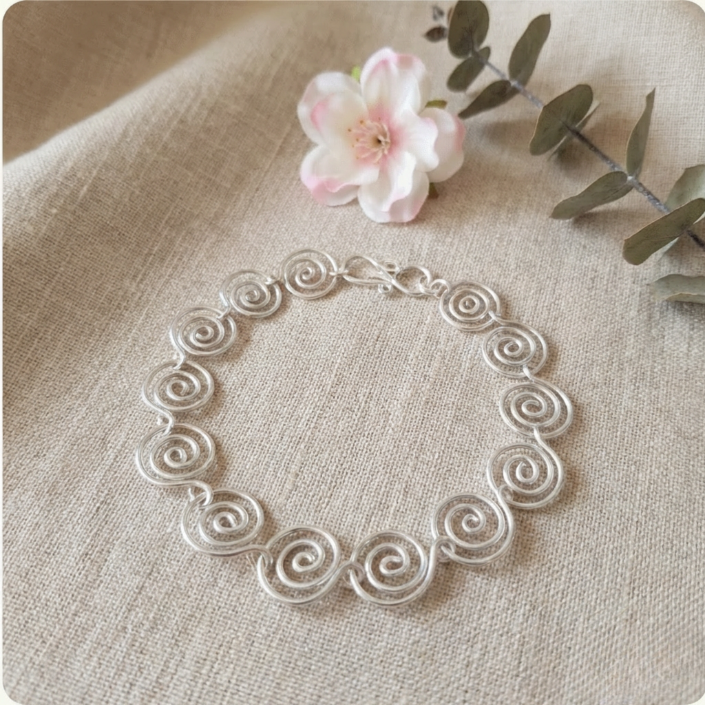 Silver bracelet with intricate design on a beige fabric background with a flower and leaves.