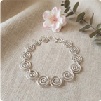 Silver bracelet with intricate design on a beige fabric background with a flower and leaves.