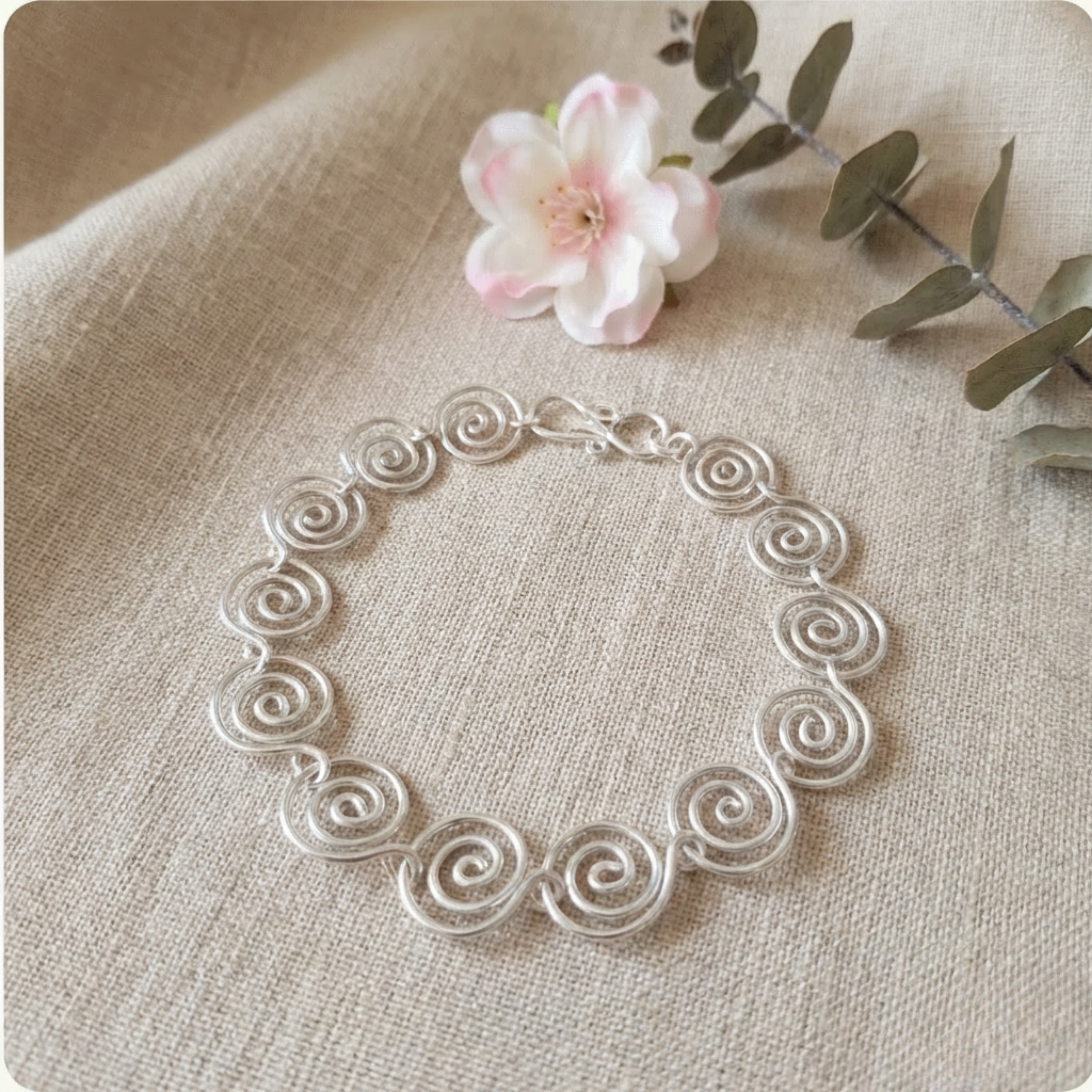 Silver bracelet with intricate design on a beige fabric background with a flower and leaves.