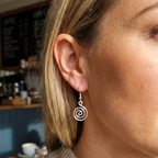 Close-up of a person wearing a spiral earring with a blurred cafe background