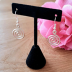 Silver spiral earrings on a black earring stand with a pink flower in the background.