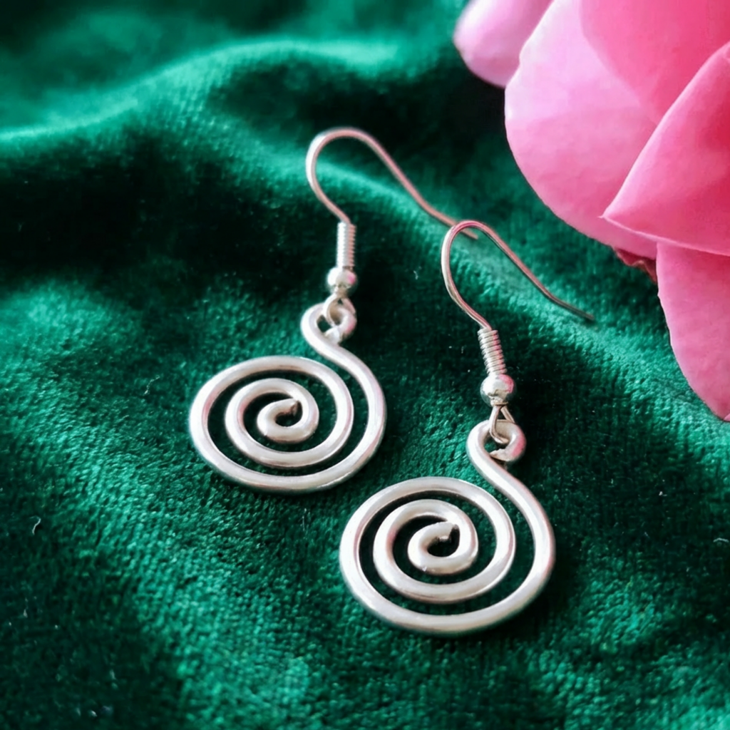 Silver spiral earrings on a green fabric background with a pink flower.