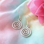 Silver spiral earrings on a soft pink and green fabric background