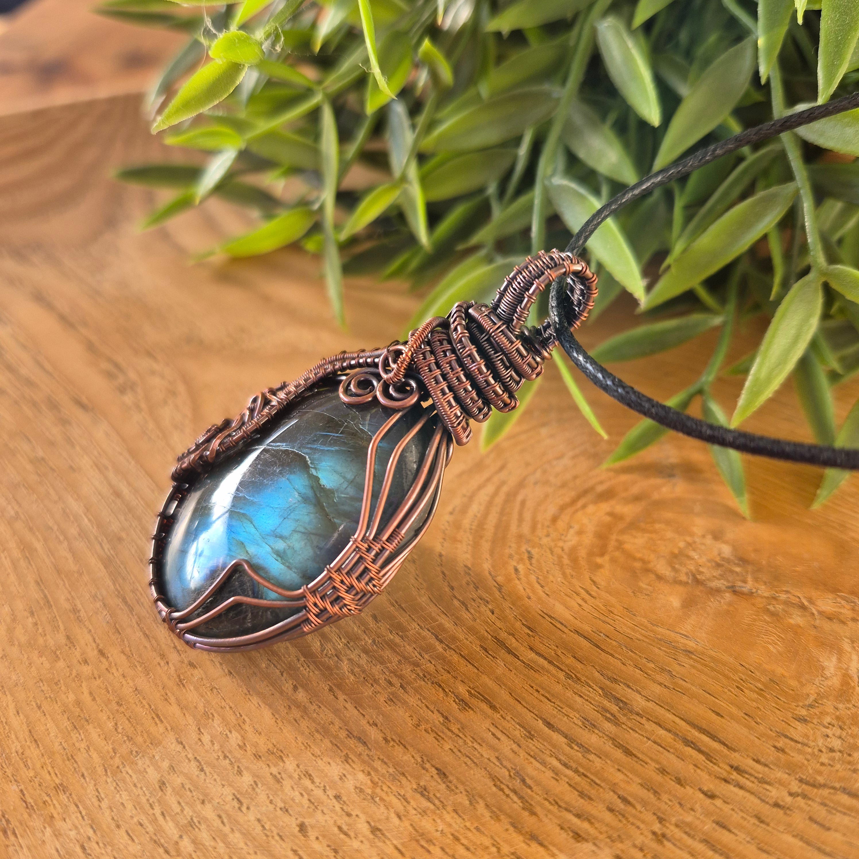 Necklace with a blue stone pendant on a wooden surface with green leaves in the background