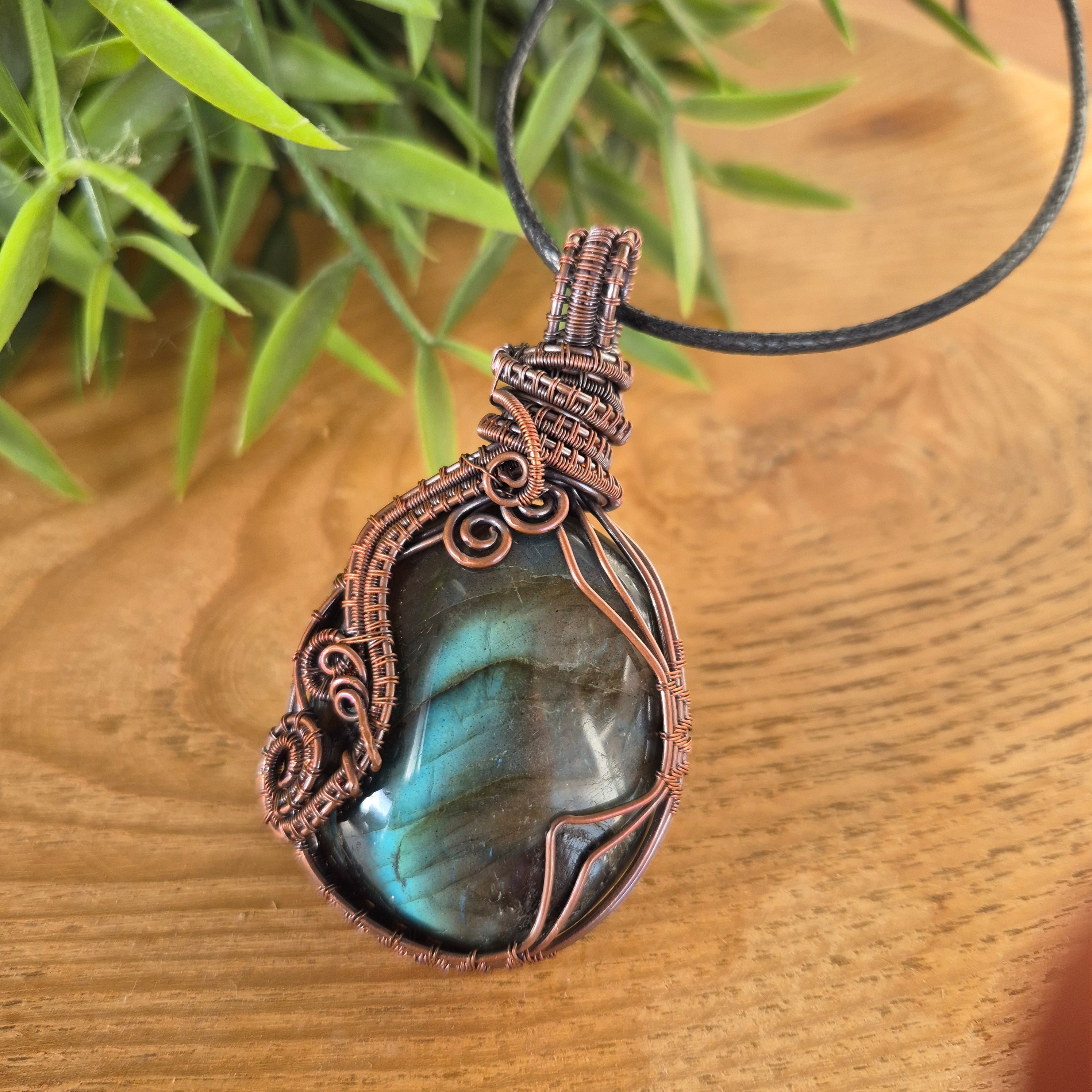 Copper-wrapped pendant with a labradorite stone on a wooden surface with greenery.