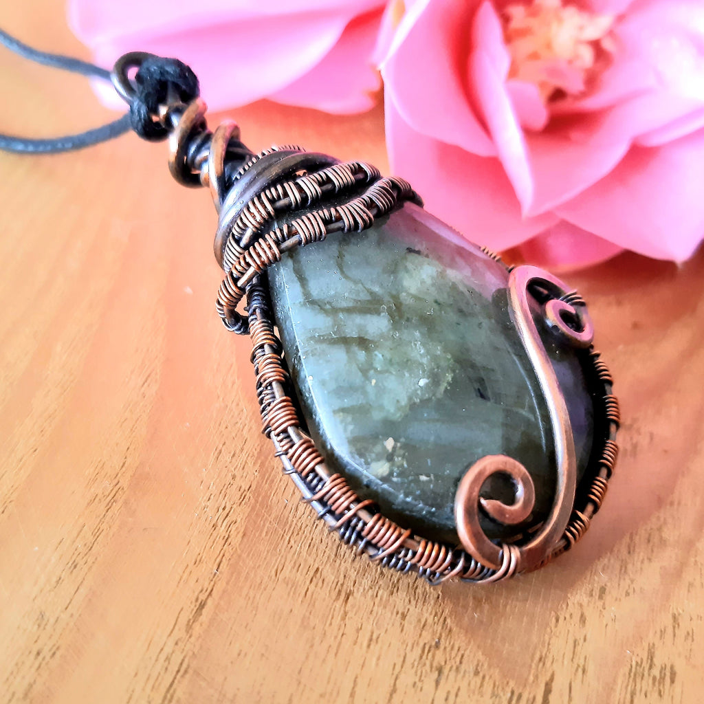 Jewelry with a green stone pendant on a wooden surface with pink flowers.