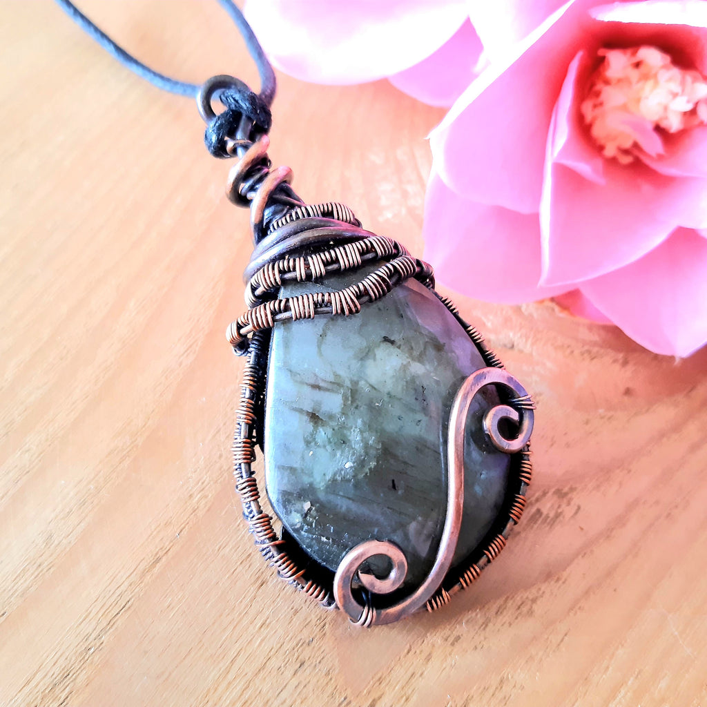Copper wire wrapped Labradorite pendant with a Celtic spiral on a wooden surface