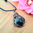 Necklace with a blue pendant on a wooden surface with a pink flower.