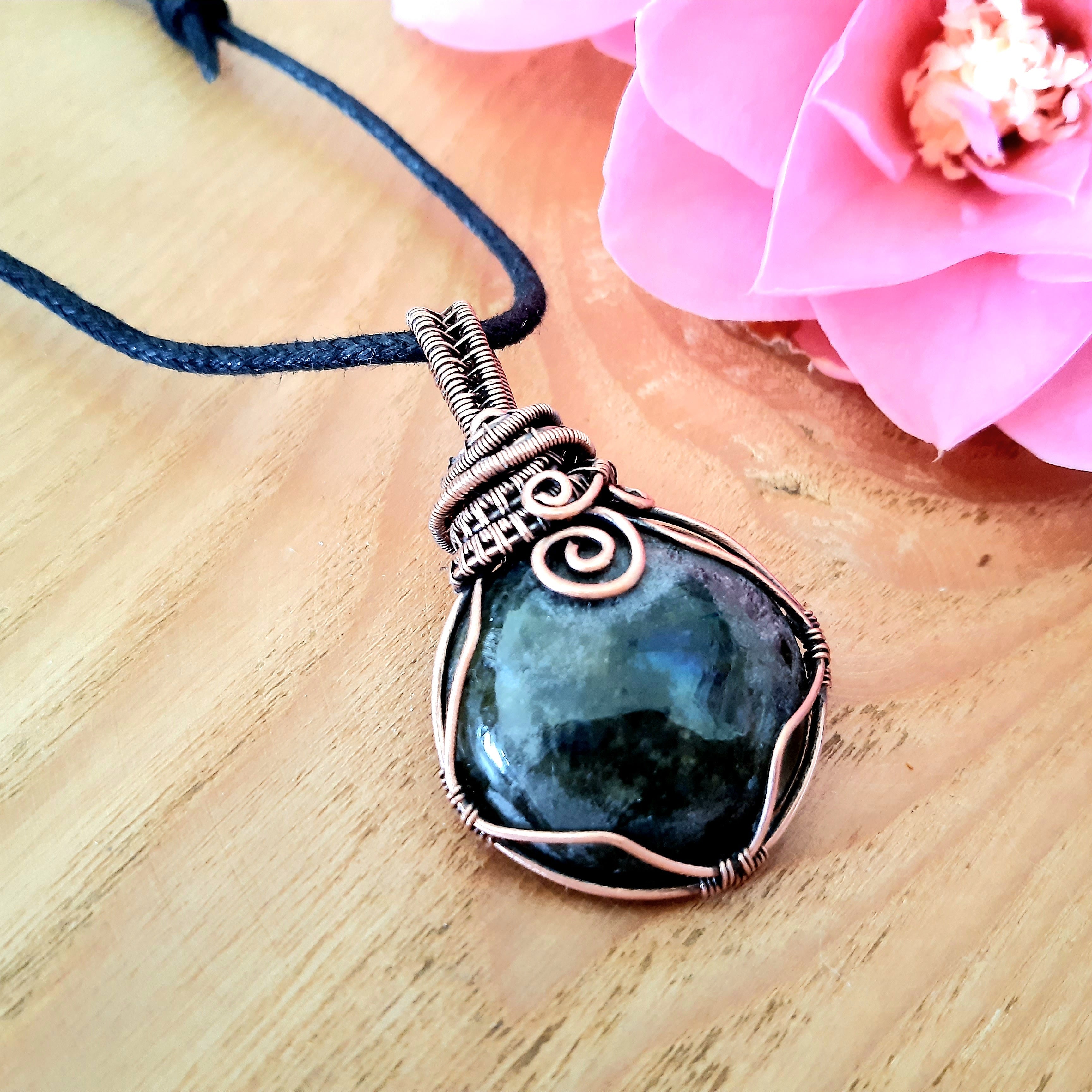 Necklace with a blue pendant on a wooden surface with a pink flower.