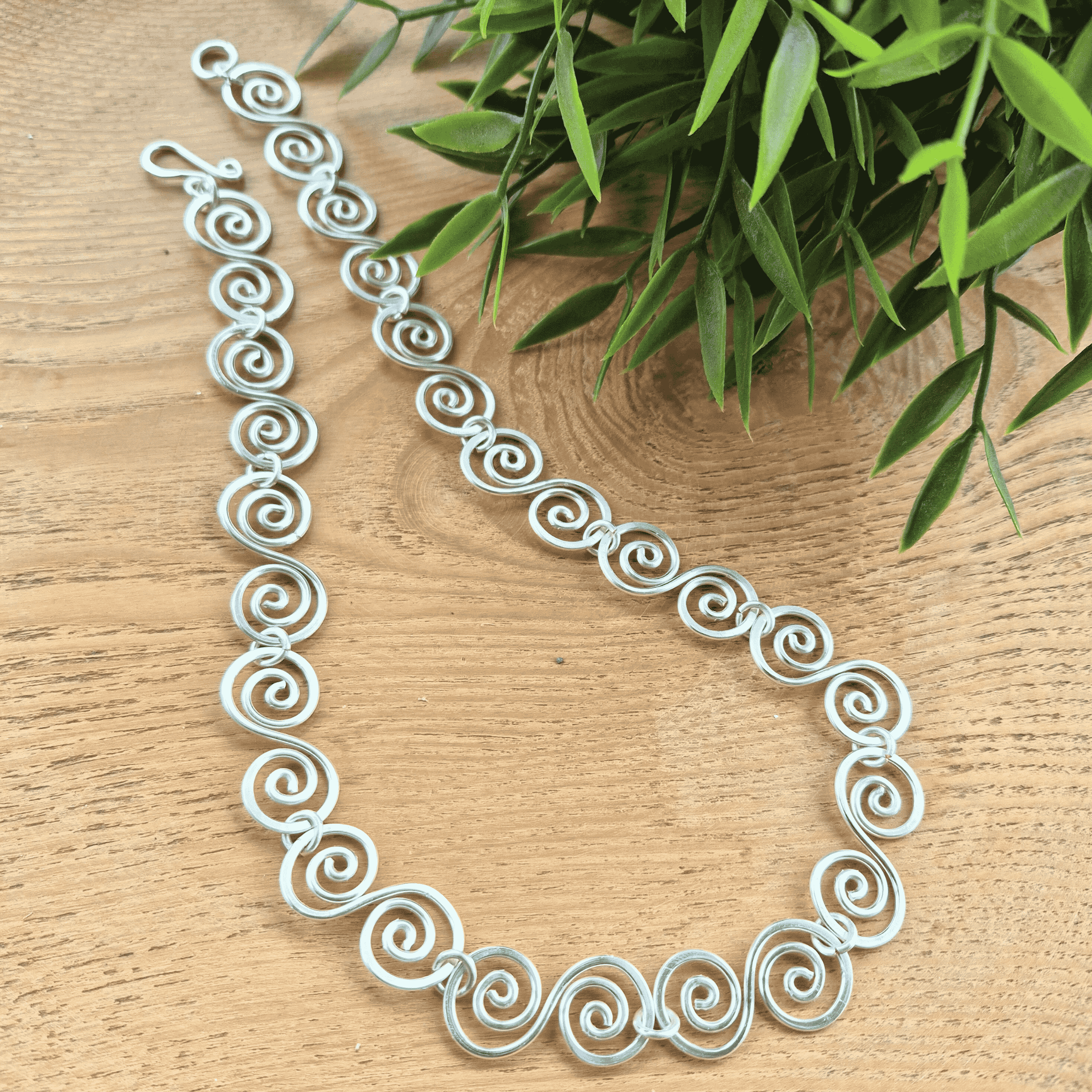 Silver spiral necklace on a wooden surface with green leaves