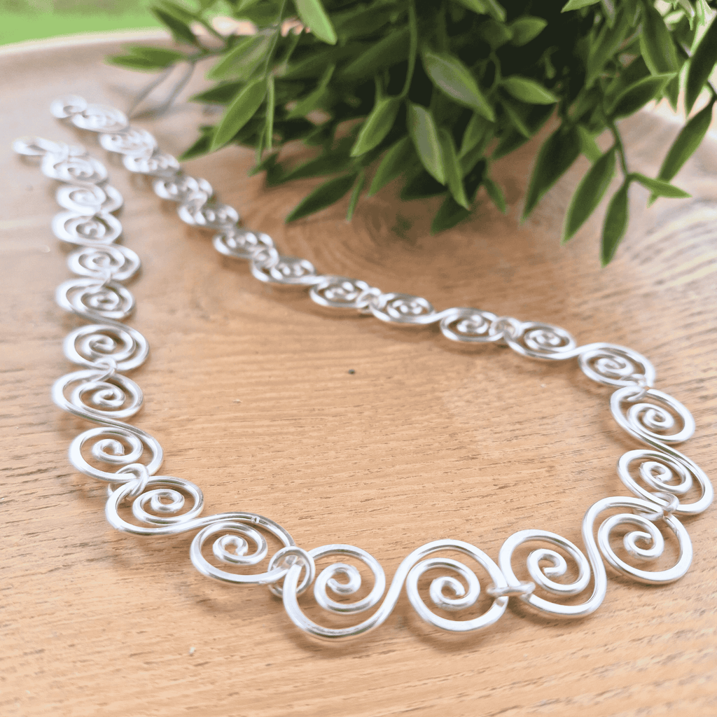 Silver necklace with intricate designs on a wooden surface with green leaves in the background