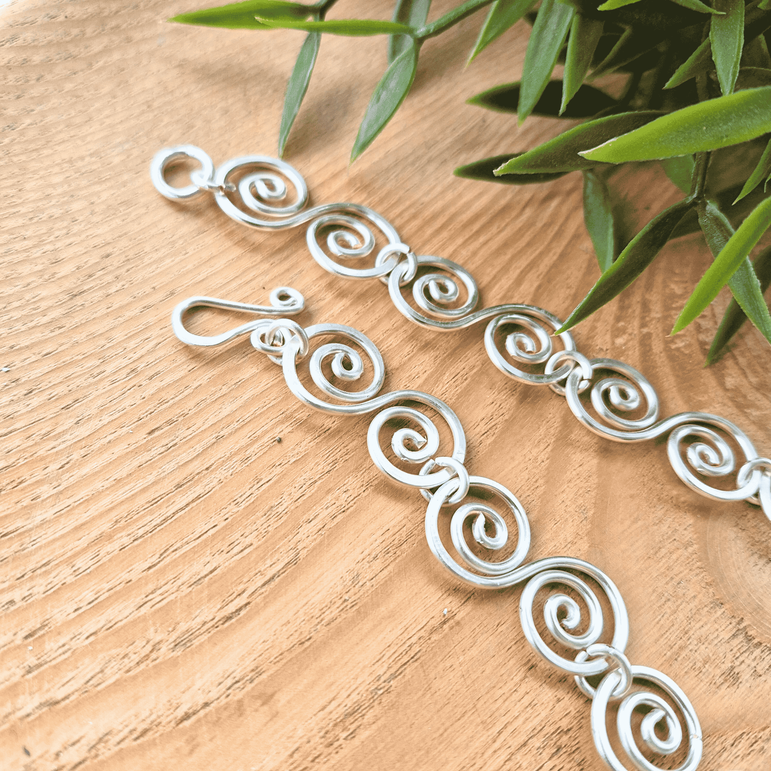 Silver necklace with intricate designs on a wooden surface with green leaves in the background