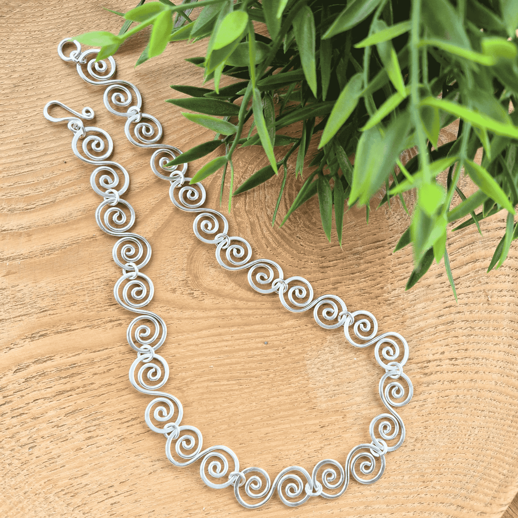 Silver spiral necklace on a wooden surface with green leaves