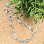 Silver spiral necklace on a wooden surface with green leaves