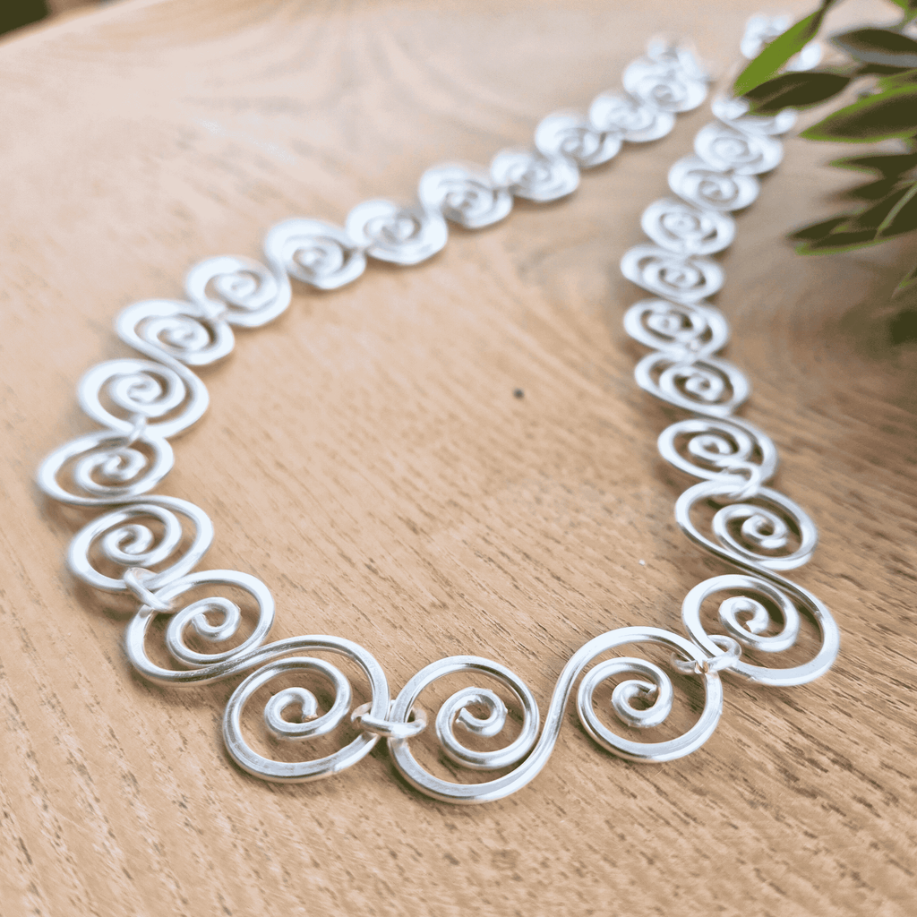 Silver necklace with intricate designs on a wooden surface close up view of the spirals