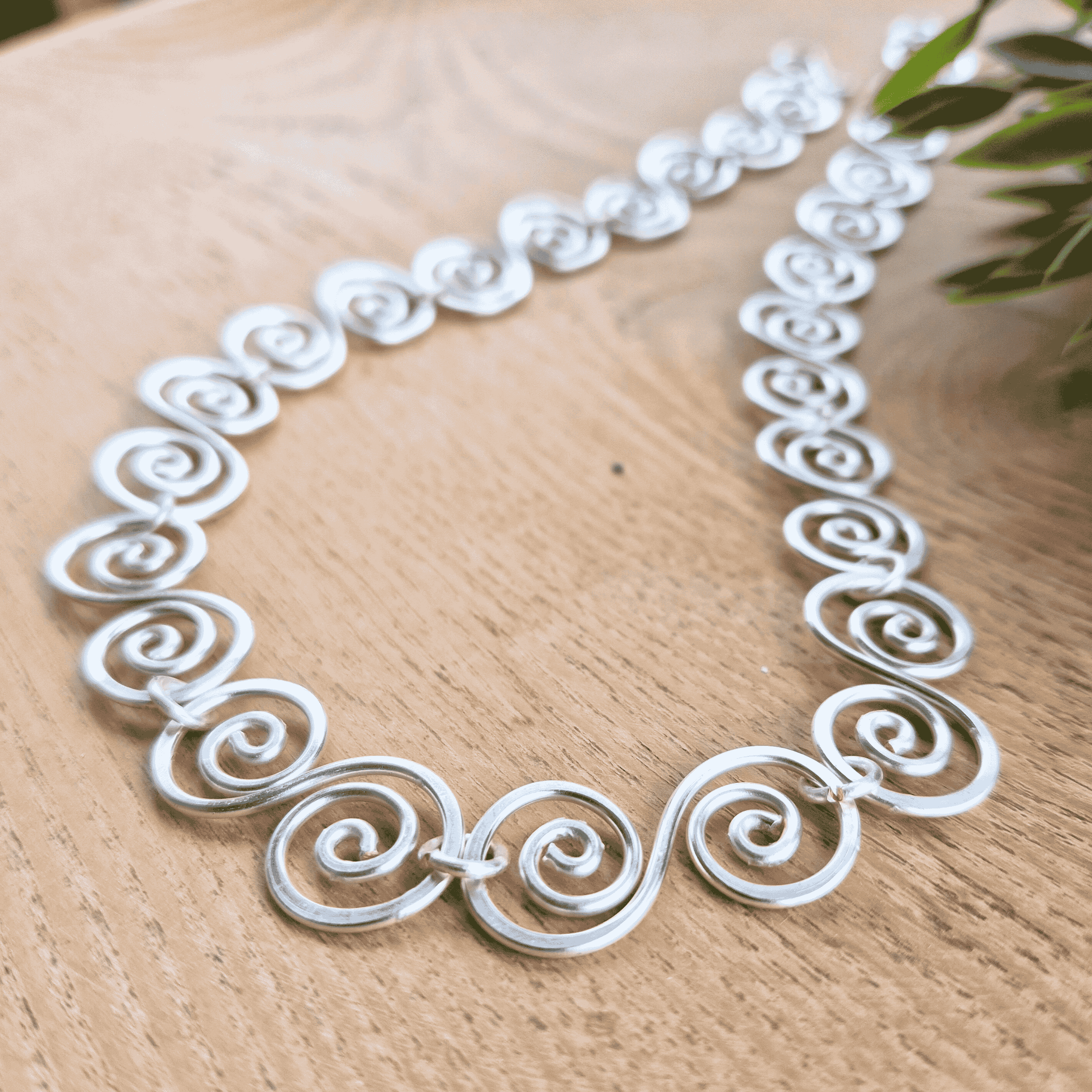 Silver necklace with intricate designs on a wooden surface close up view of the spirals