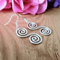 Spiral design earrings on a wooden surface with pink flowers in the background