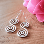 White spiral earrings on a wooden surface with pink flowers in the background