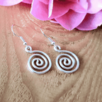 Silver spiral earrings on a wooden surface with pink flowers in the background