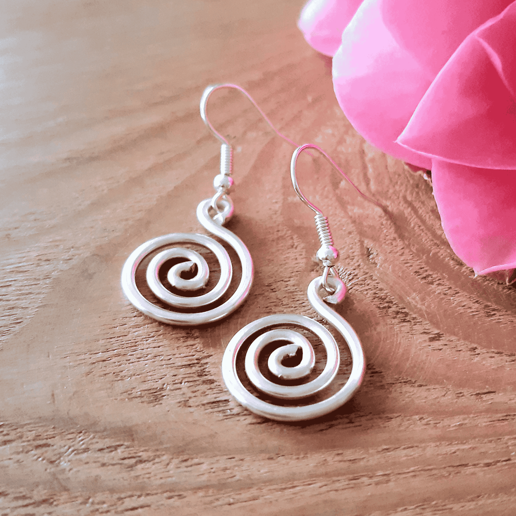 White spiral earrings on a wooden surface with pink fabric in the background