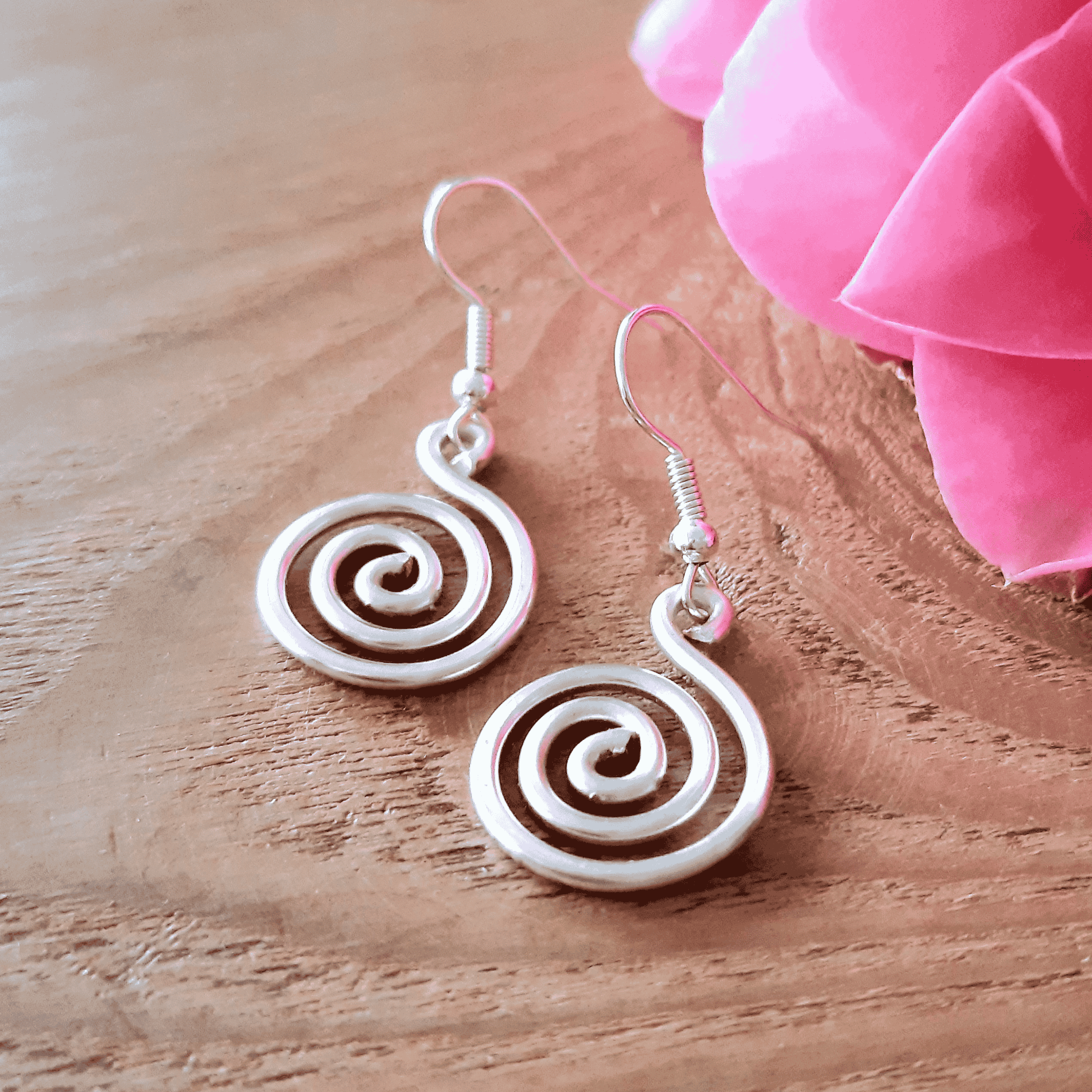 White spiral earrings on a wooden surface with pink fabric in the background