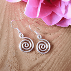 Silver spiral earrings on a wooden surface with pink flowers in the background