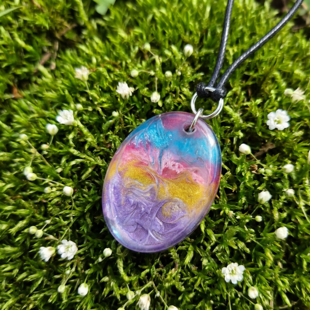 Colorful marbled pendant on a black cord against a green moss background with small white flowers.