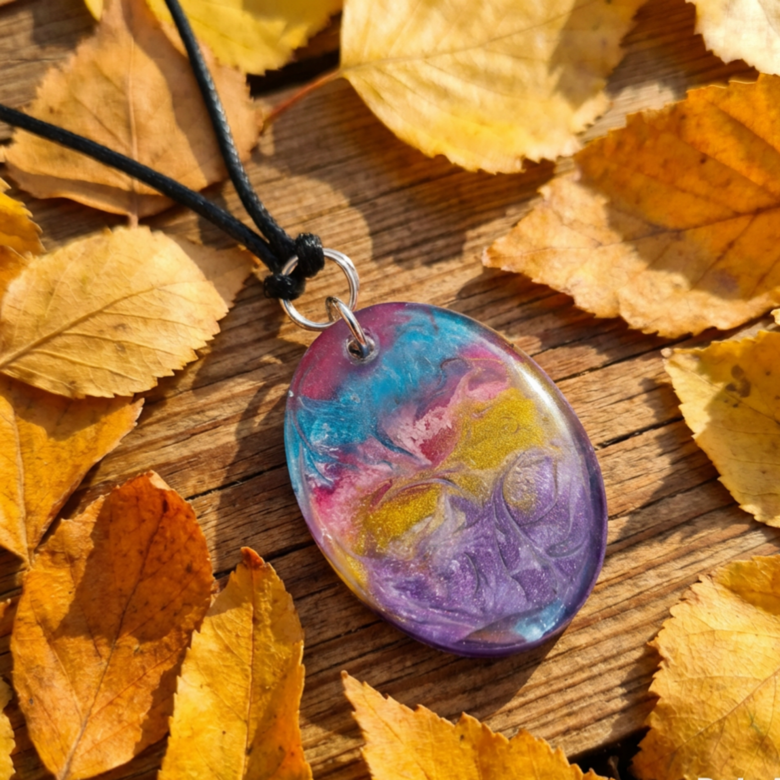 Colorful marbled pendant necklace on a wooden surface with autumn leaves