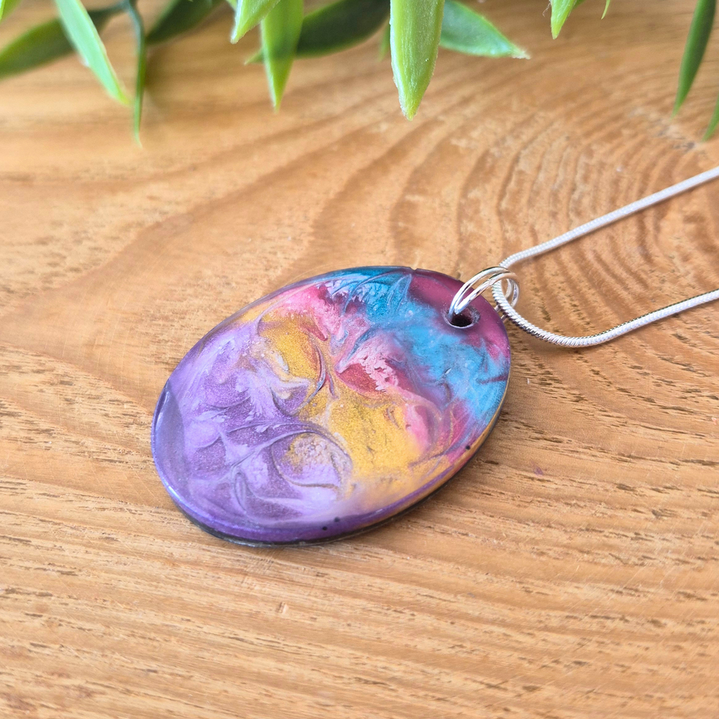 Colorful pendant on a wooden surface with green leaves in the background