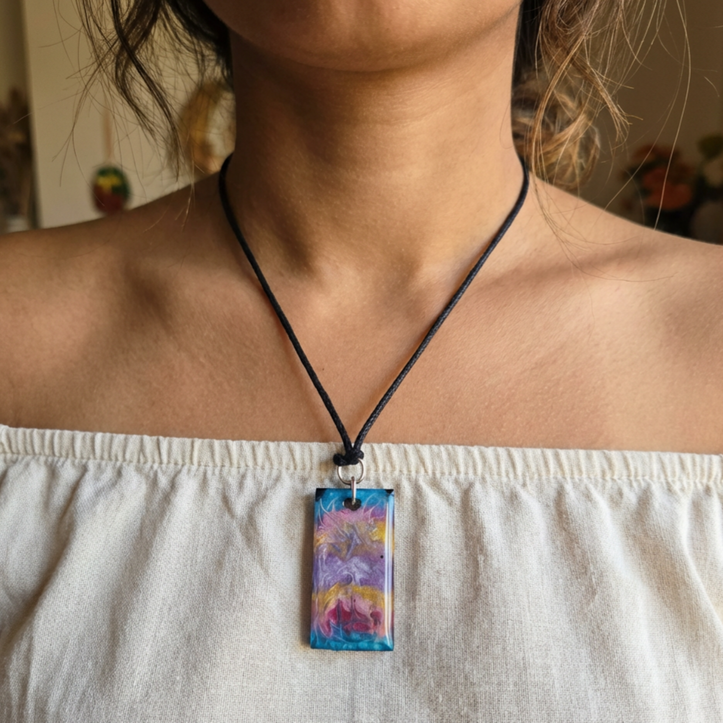 Person wearing a necklace with a colorful pendant, blurred background