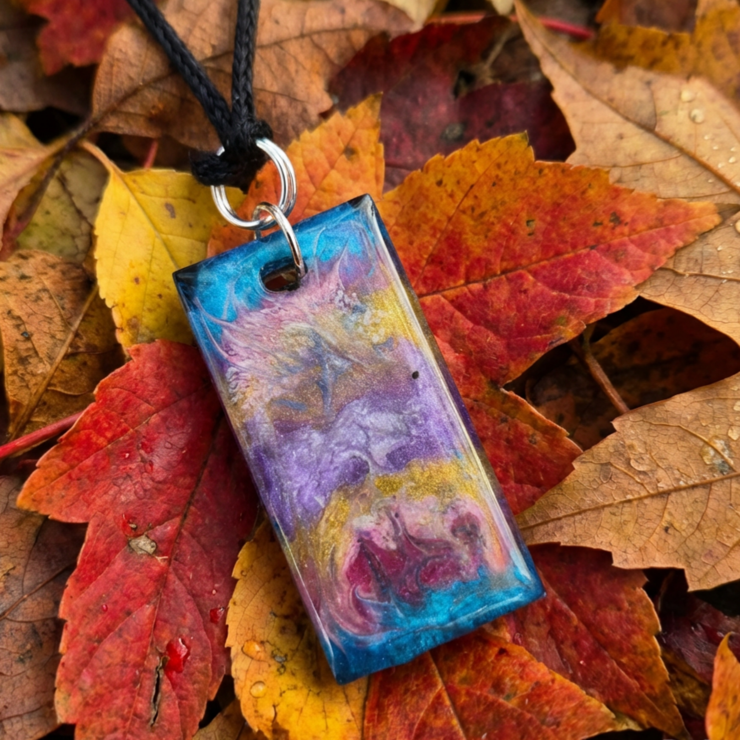 Colorful marbled pendant on a black cord with autumn leaves in the background