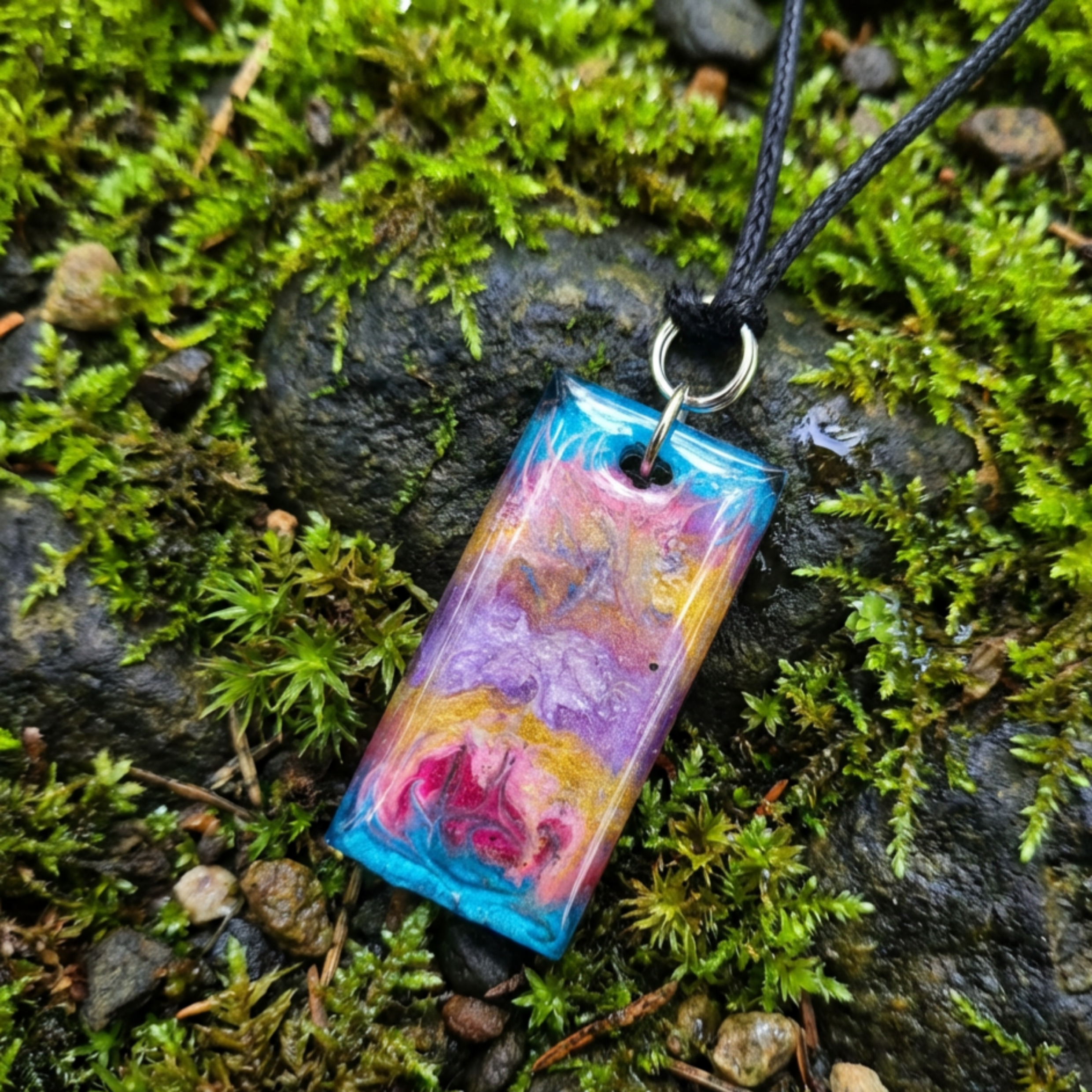 Colorful rectangular pendant on a black cord lying on green moss