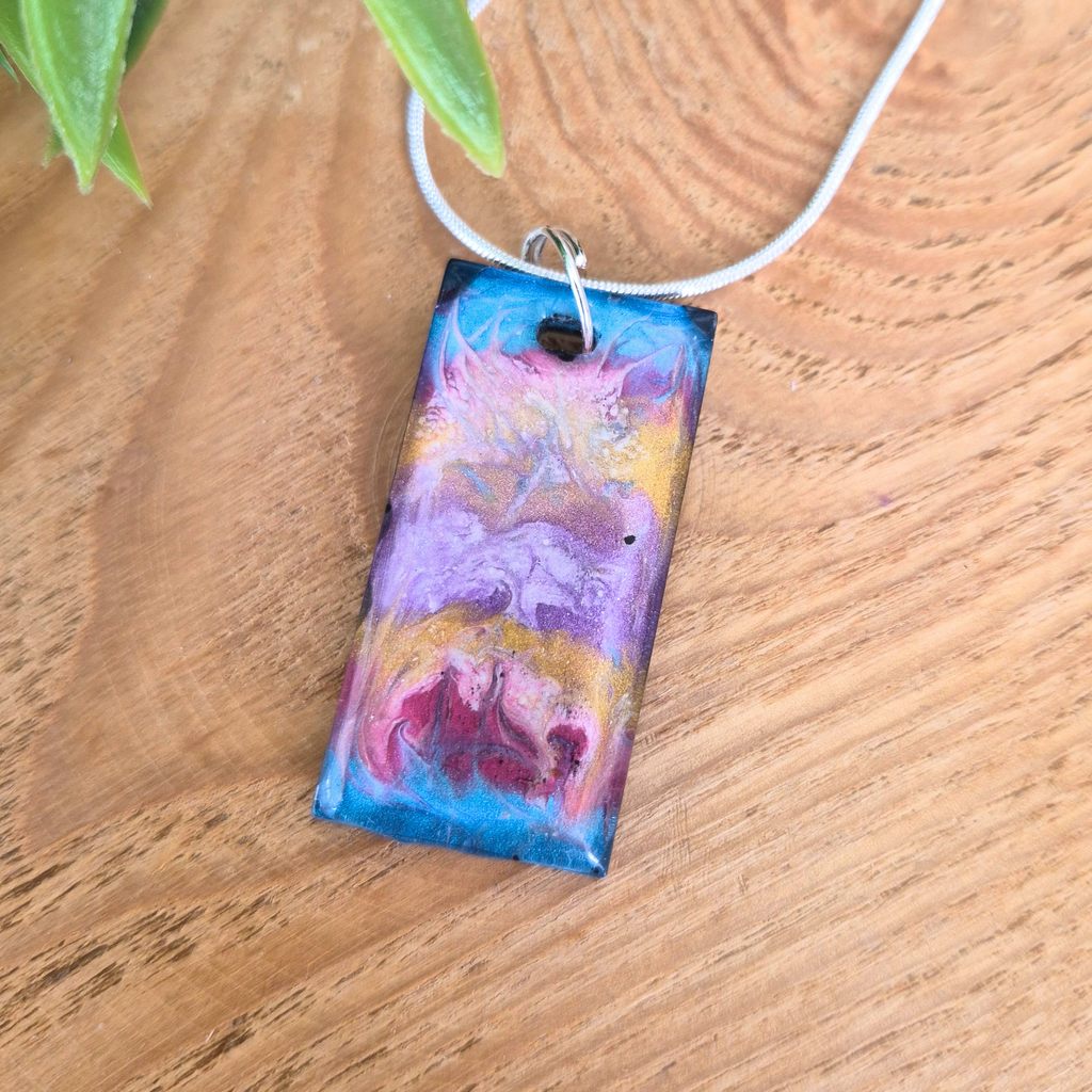 Colorful rectangular pendant on a wooden surface with green leaves