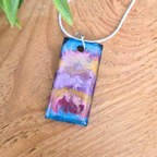 Colorful rectangular pendant on a wooden surface with green leaves