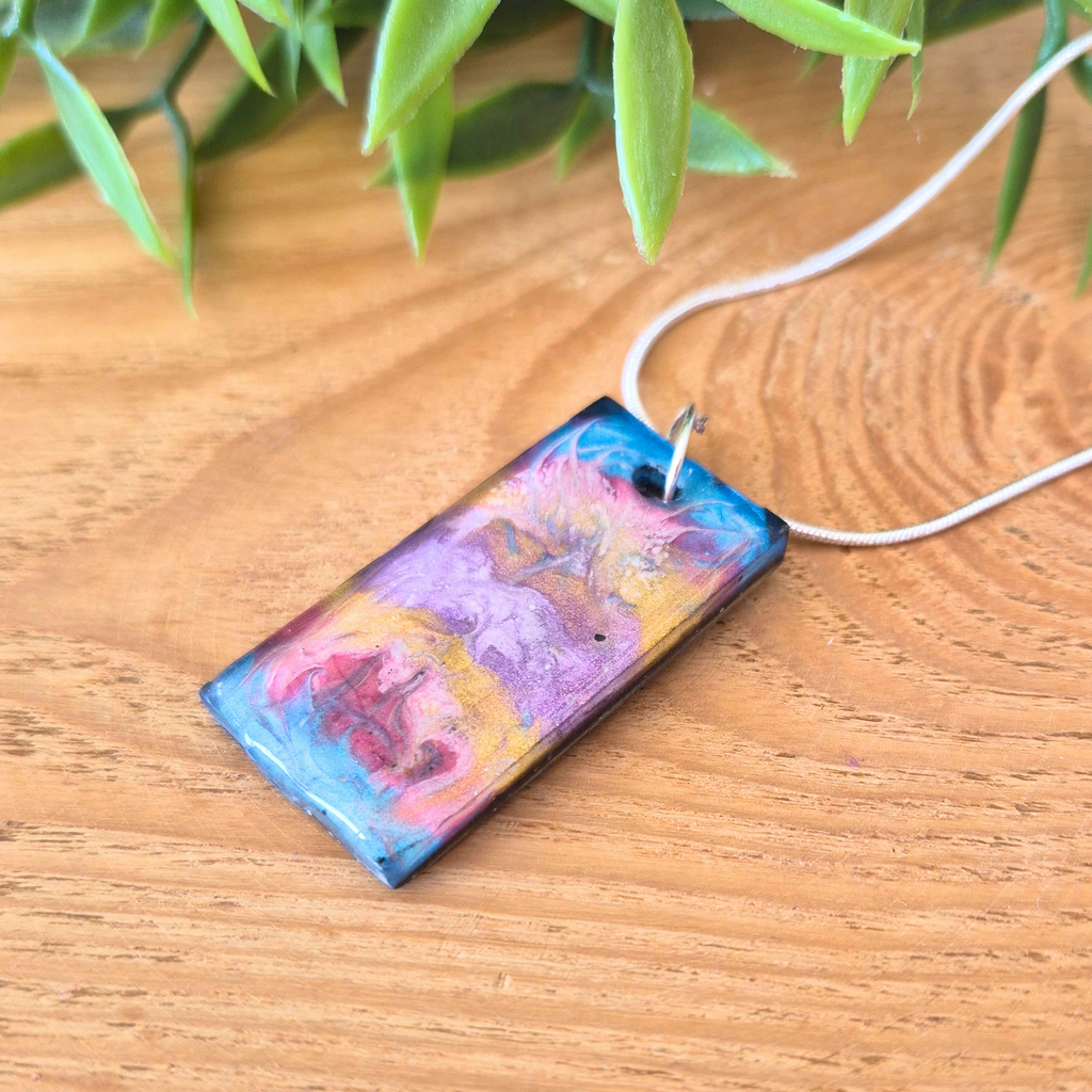 Rectangle pendant with blue, gold, pink and purple colours on a wooden surface