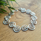 Celtic silver spiral bracelet n a wooden surface with foliage